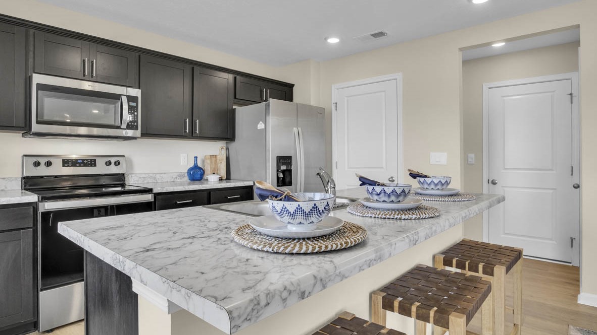 Kitchen island with laminate countertop, blue and white bowls, leather stools, and stainless steel appliances in the background