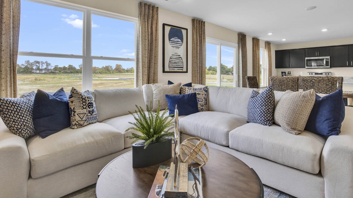 Living room with beige couch, blue throw pillows, and coffee table with plans