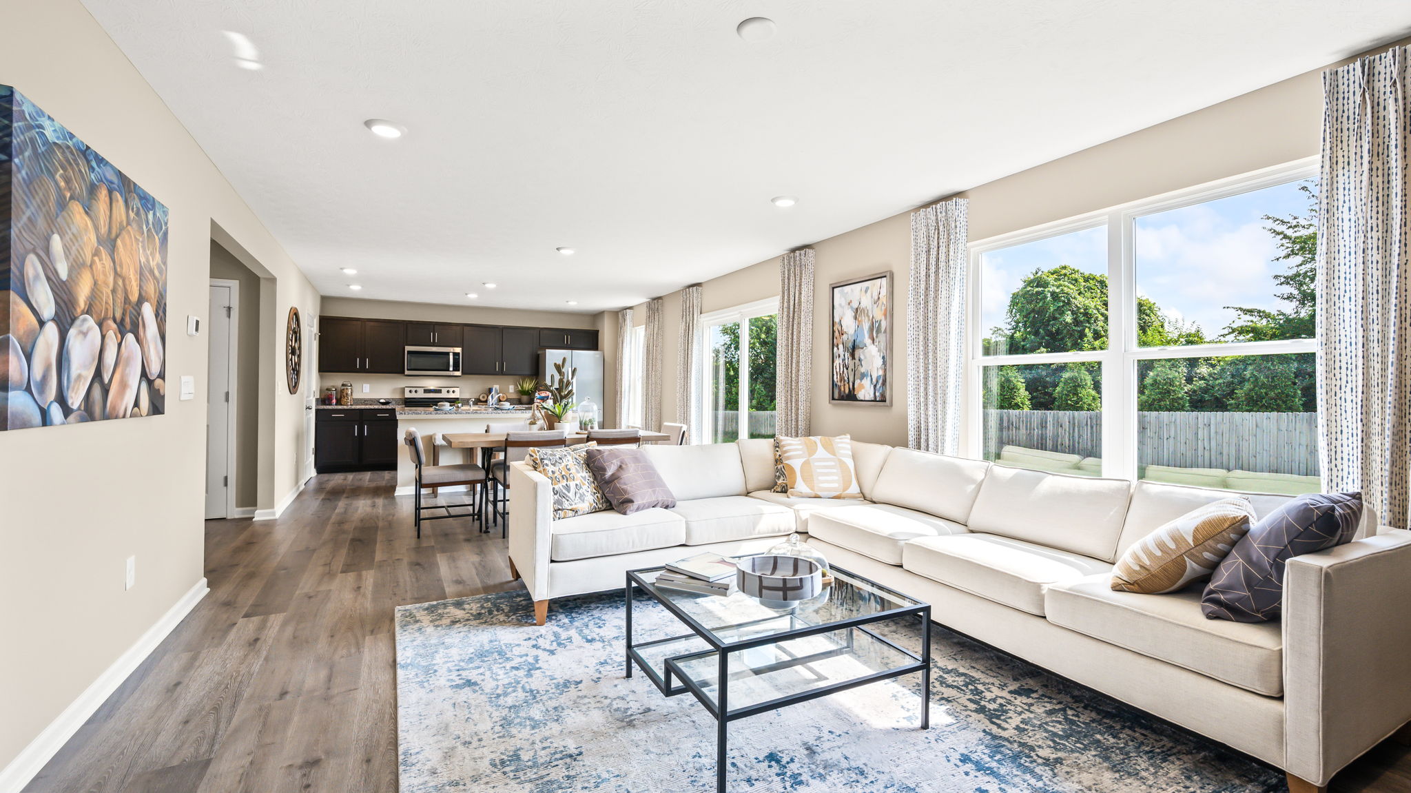 Open-plan living room with a white sectional and glass coffee table, extending past the dining area to the kitchen.