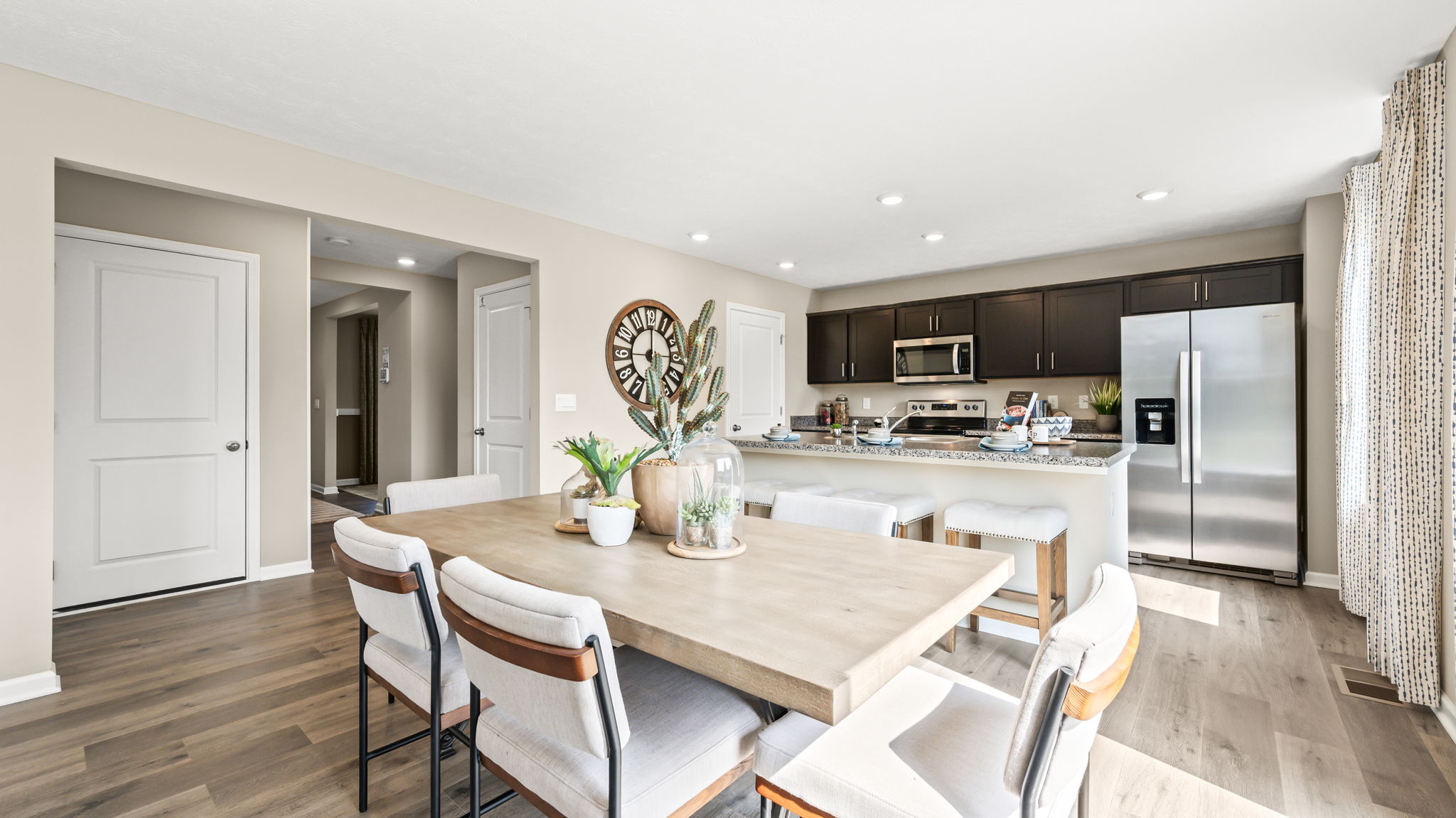 Wide open-plan view with a central dining table, kitchen breakfast bar and stools to the left, and living room to the right.
