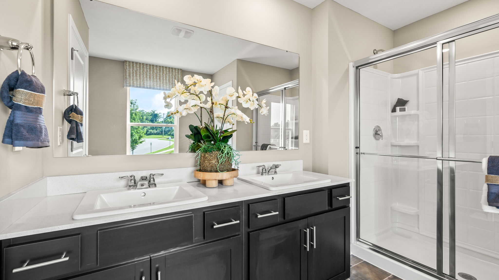Tiled bathroom hallway with a window, towel rack, small bench, white paneled door, and a glass shower visible at the far end.