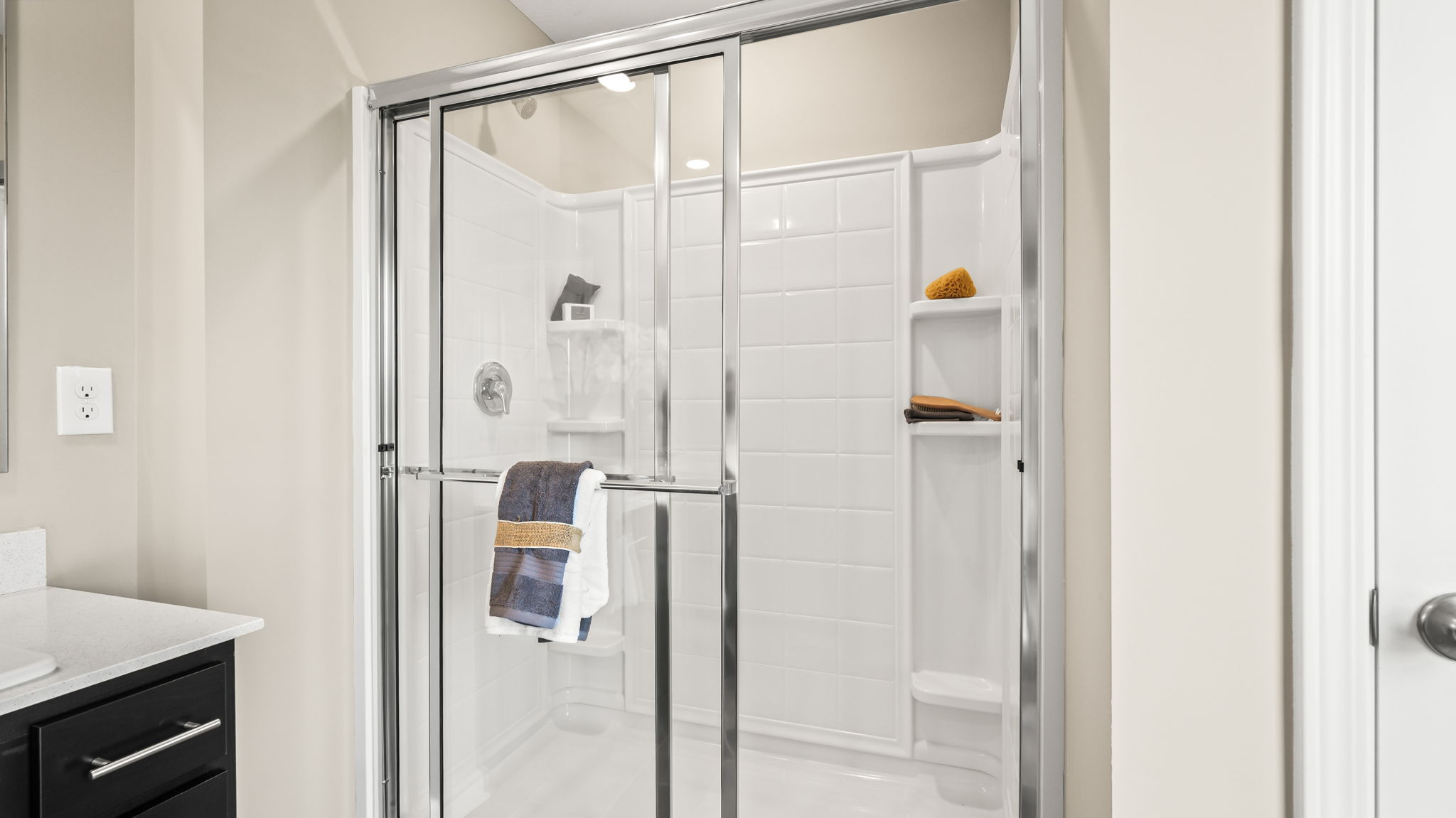 Primary bathroom with a dark double-sink vanity, large wall mirror, white orchid arrangement, and glass-enclosed shower.