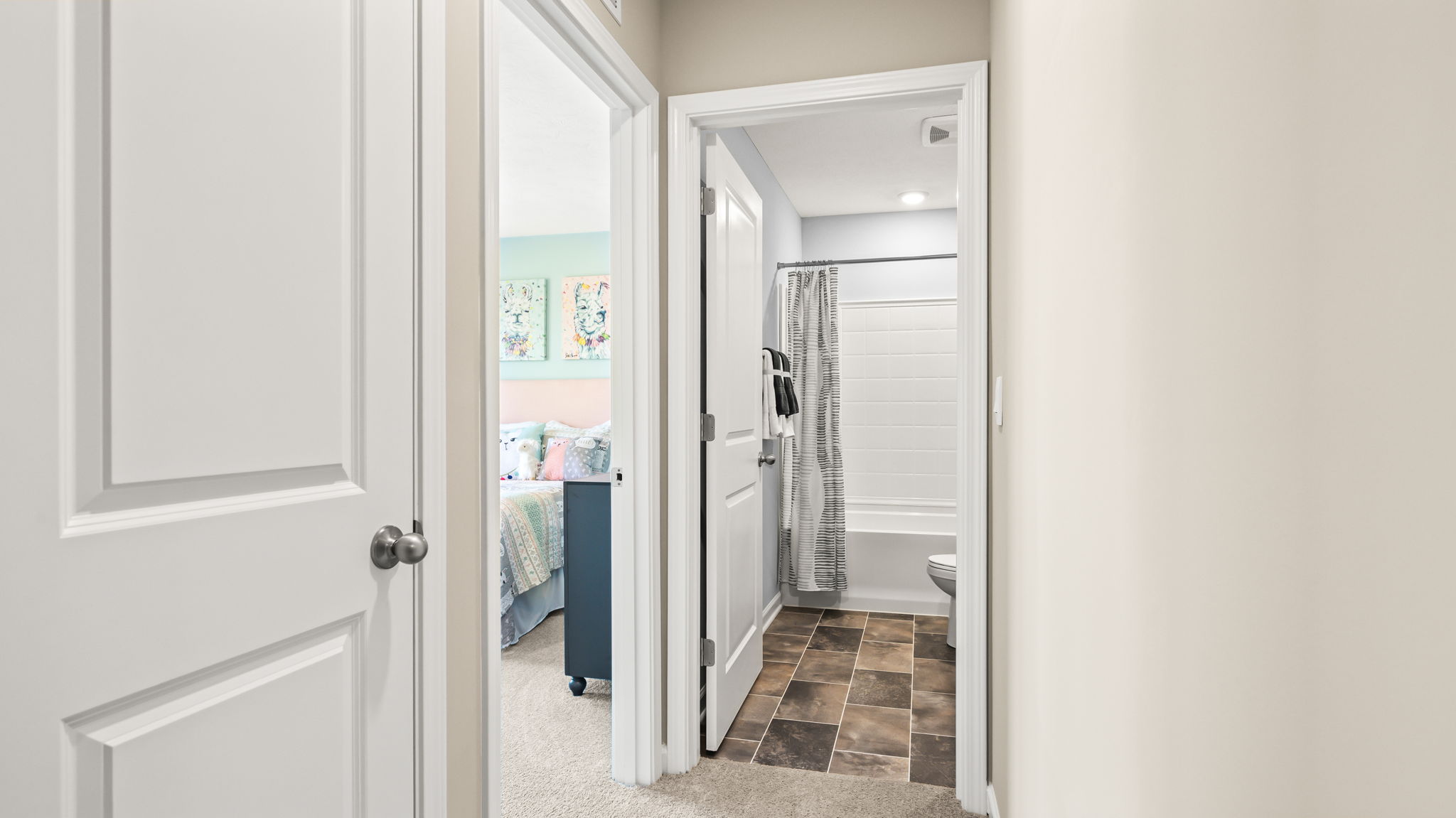 Primary bathroom with a long dark vanity, two white sinks, large wall mirror, tiled floor, window, and central white paneled door.
