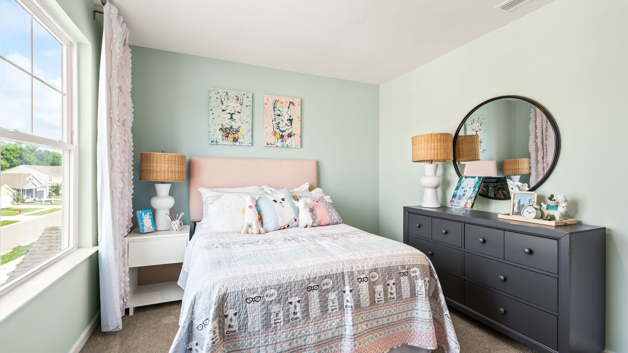Mint-green bedroom with a pink upholstered headboard, patterned bedding, ruffled curtains, twin animal prints, and a dark dresser.