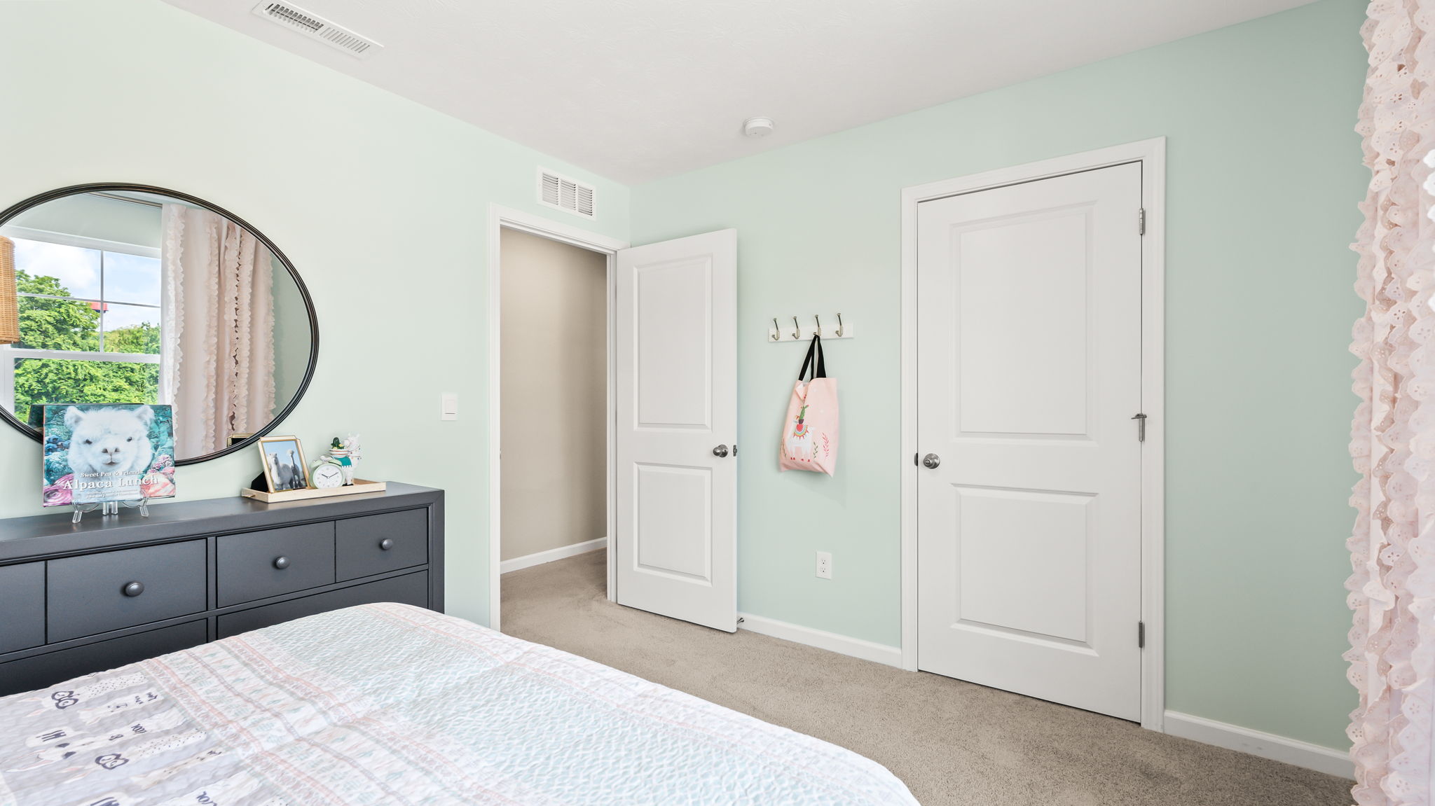 Mint-green bedroom with a patterned bed, pink headboard, dark dresser, round mirror, wicker-shade lamps, and animal artwork.