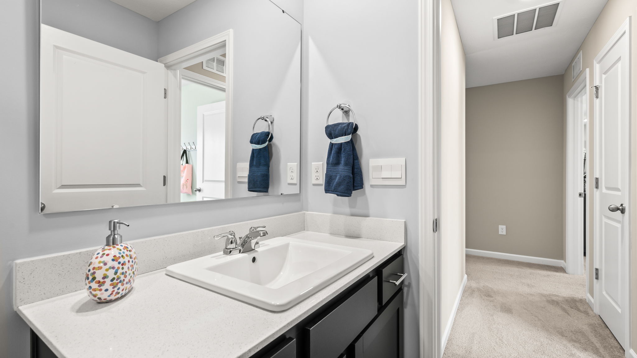 Hall bathroom with a white tub and surround, blue-striped shower curtain, dark vanity, large mirror, and blue-and-white towels.