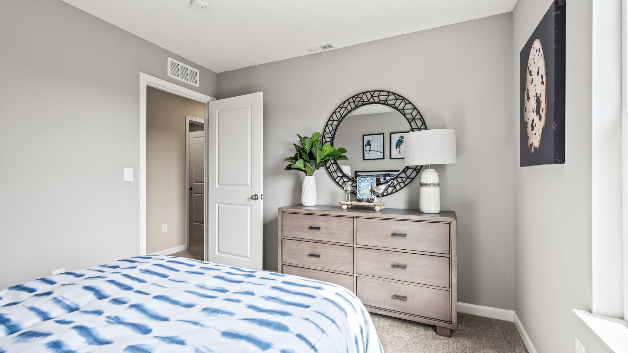 Gray bedroom with a blue-and-white bed, matching lamps, framed bird prints, egg artwork, and a white paneled closet door.