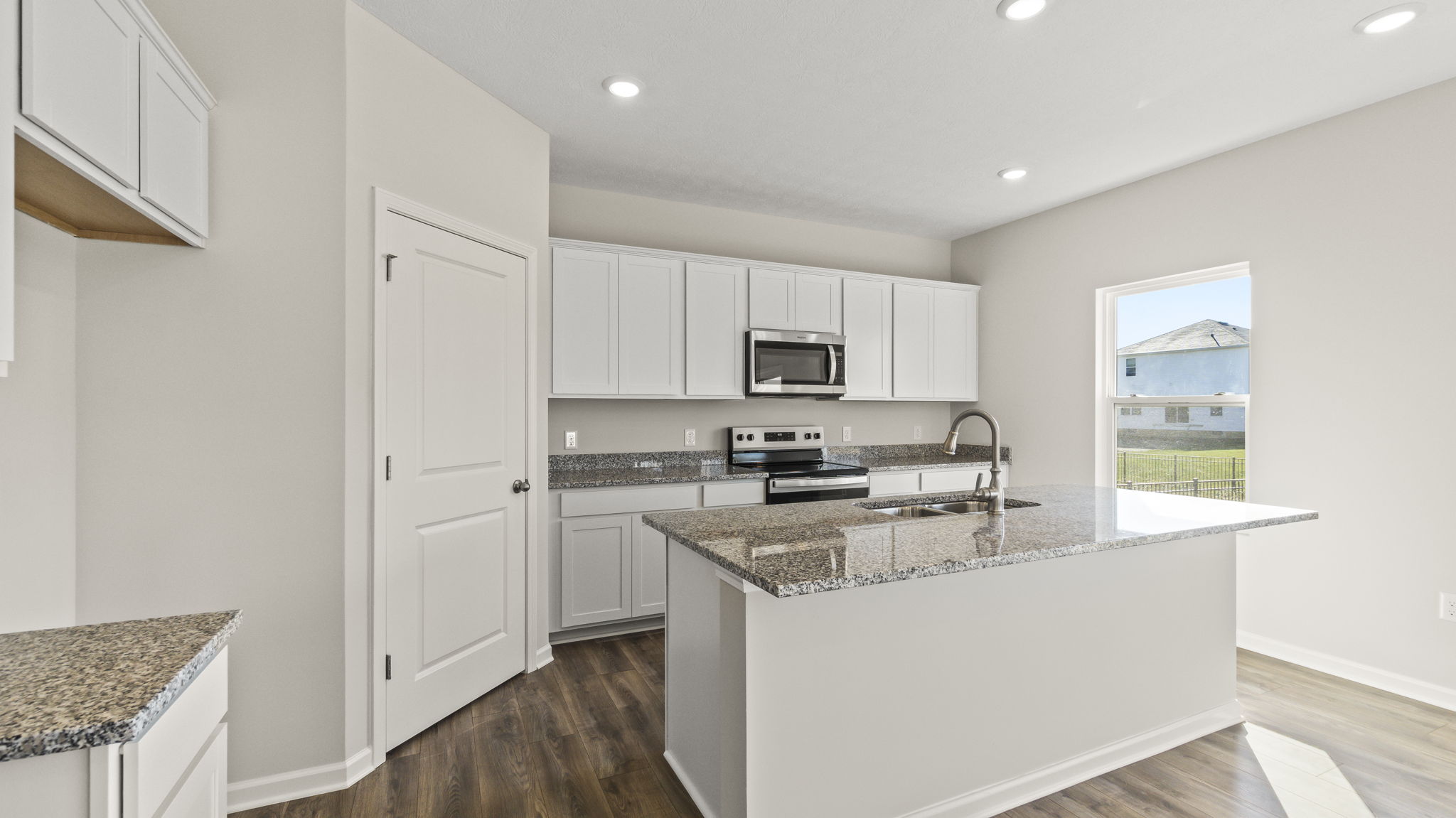 Three-quarter angle of kitchen with white cabinetry and granite countertops.