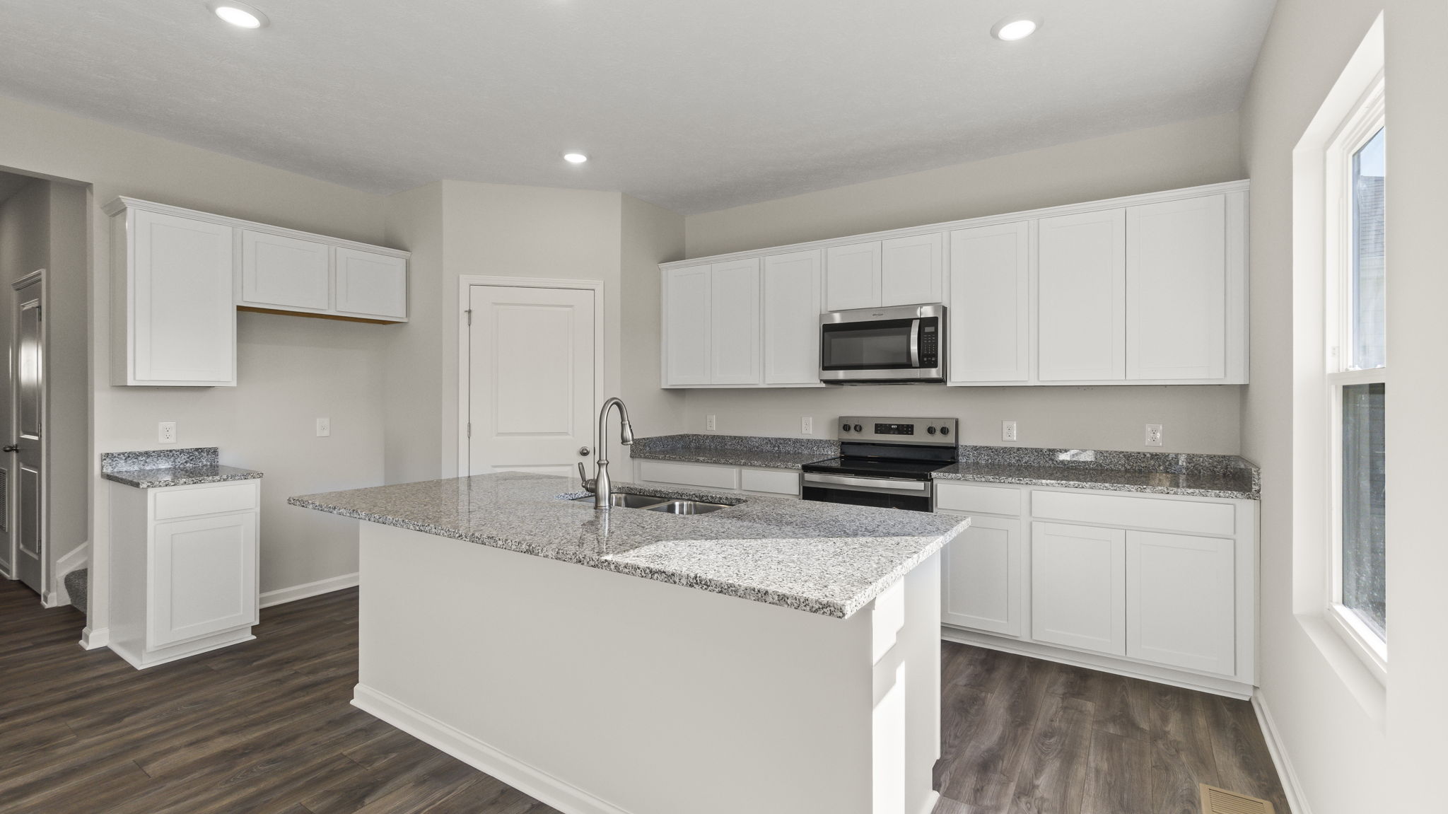 Three-quarter angle of kitchen with white cabinetry, granite countertops, and white cabinetry