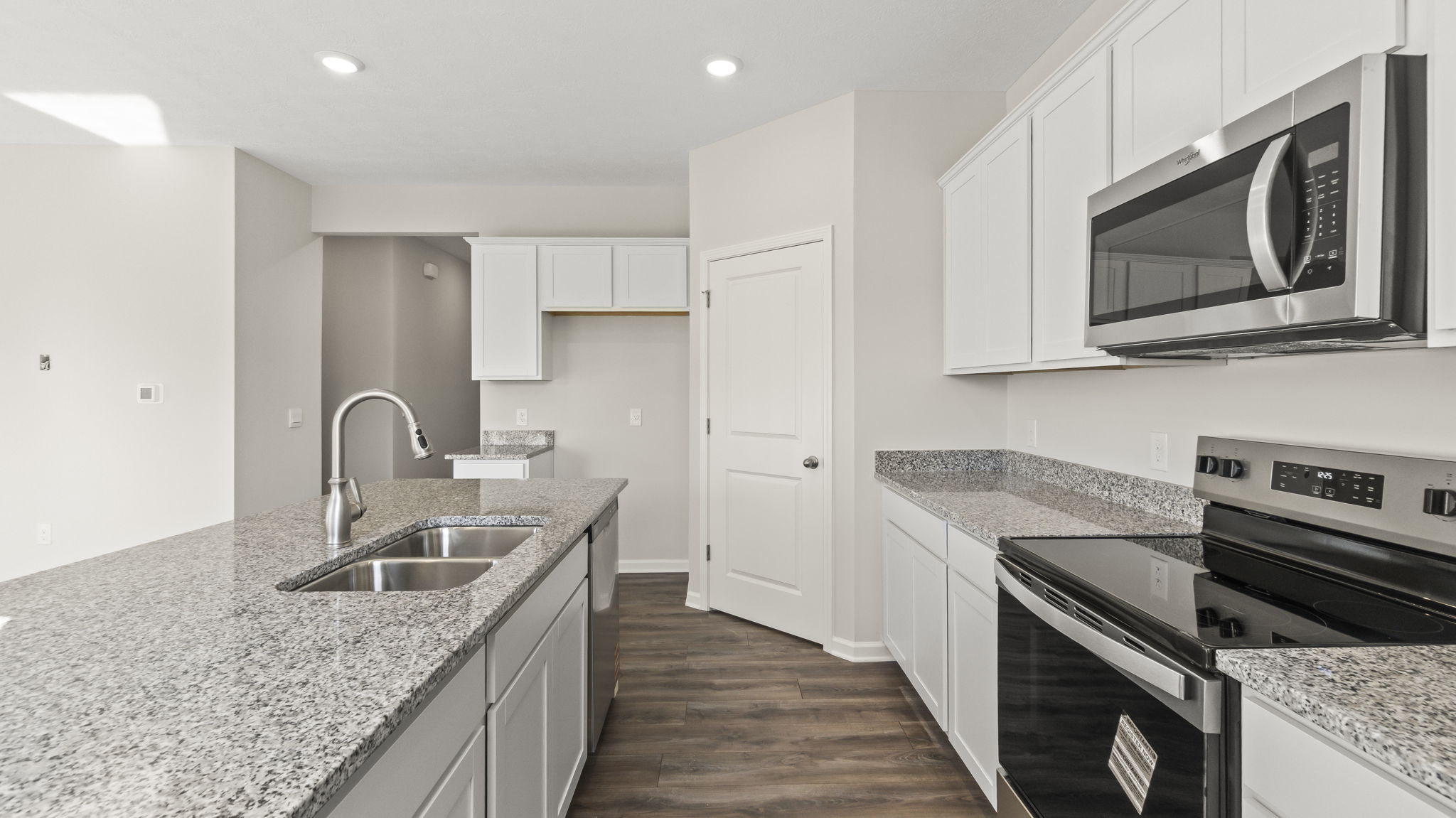 Side view of kitchen wth granite countertops, island with built-in sink and dishwasher, and door to walk-in pantry