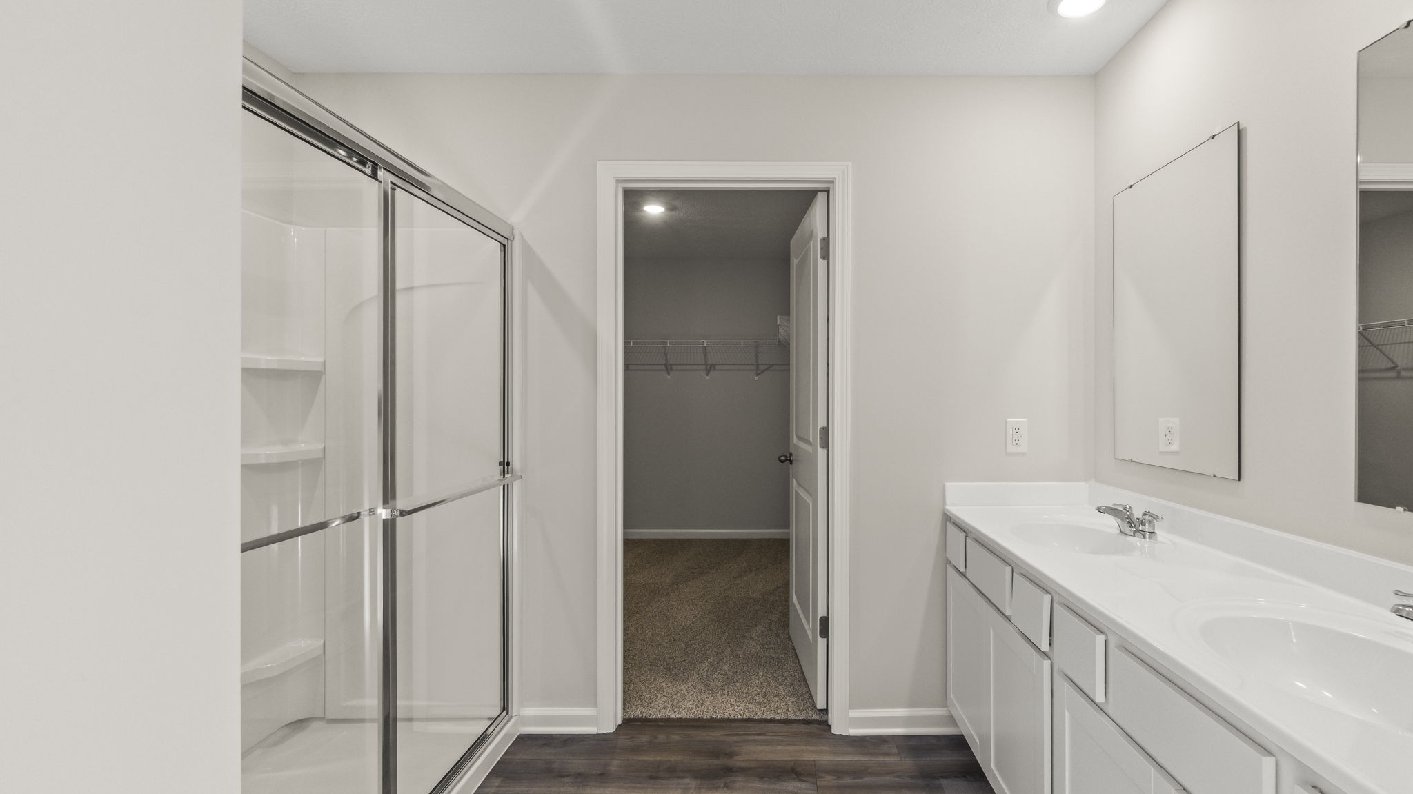 Primary bathroom suite with walk-in shower on the left, walk-in closet in the center, and dual-vanity sinks with mirror on the right.