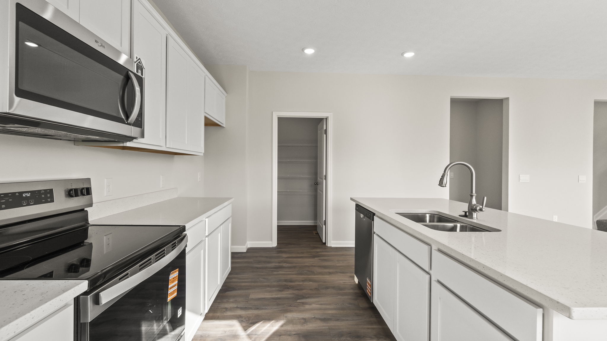 Side view of kitchen with marble countertops, island with built-in sink and dishwasher, and door to walk-in pantry