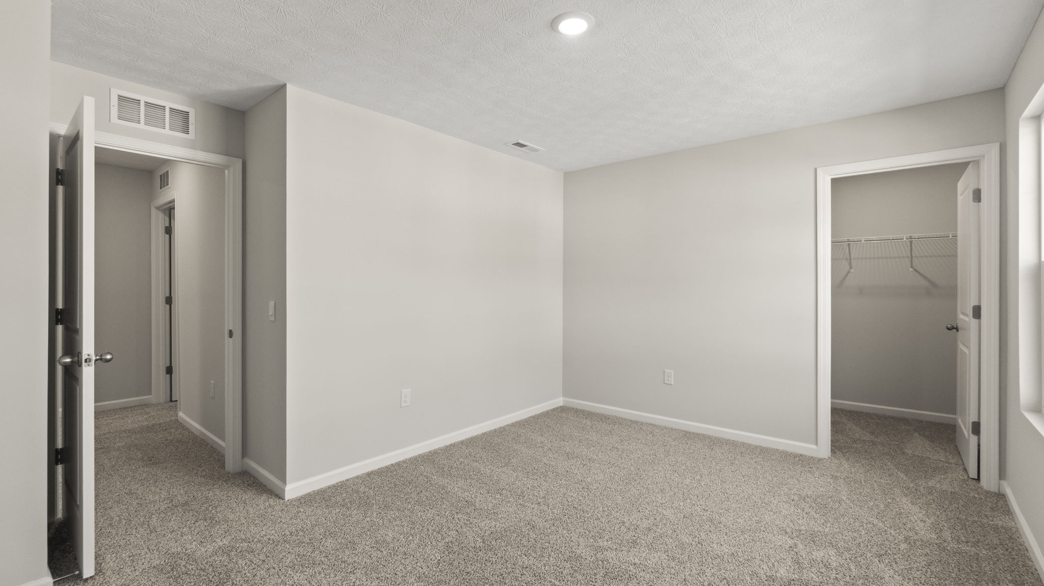 Bedroom with doors open displaying the hallway and walk-in closet with wire shelving