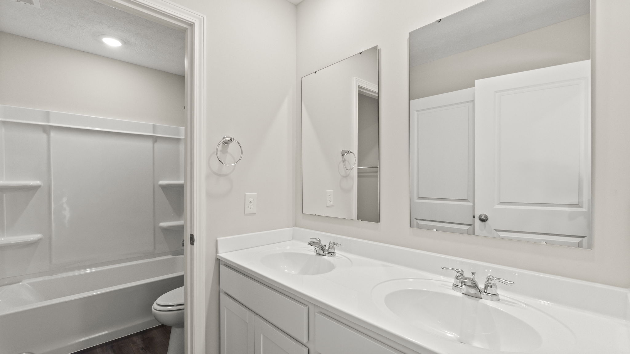 Bathroom with double-sink vanity, mirrors, and tub.