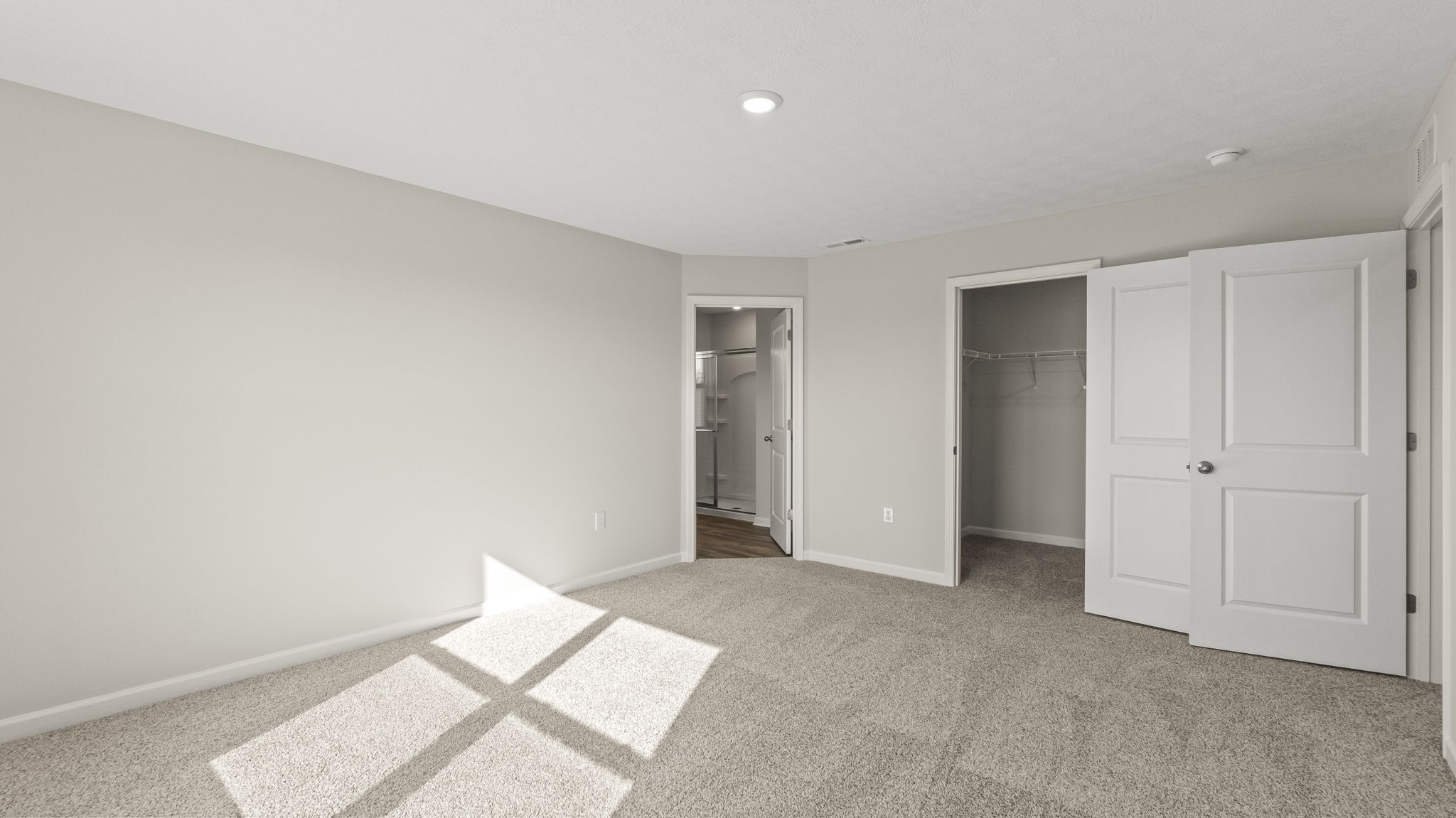 Primary bedroom with carpet, puck light, and doors open showing primary bathroom and walk-in closet.