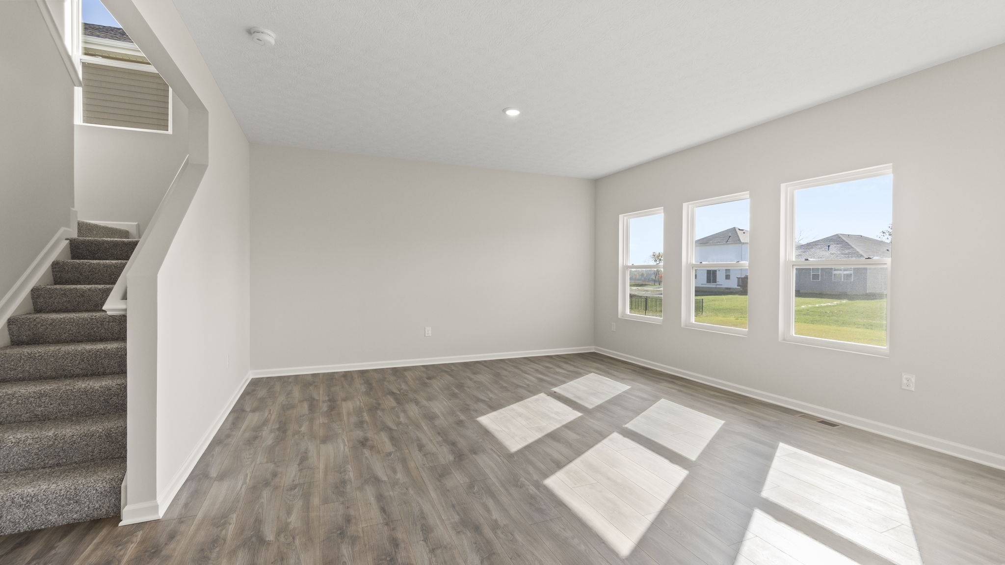 Living room with stairs to the second floor on the left and three windows on the right.