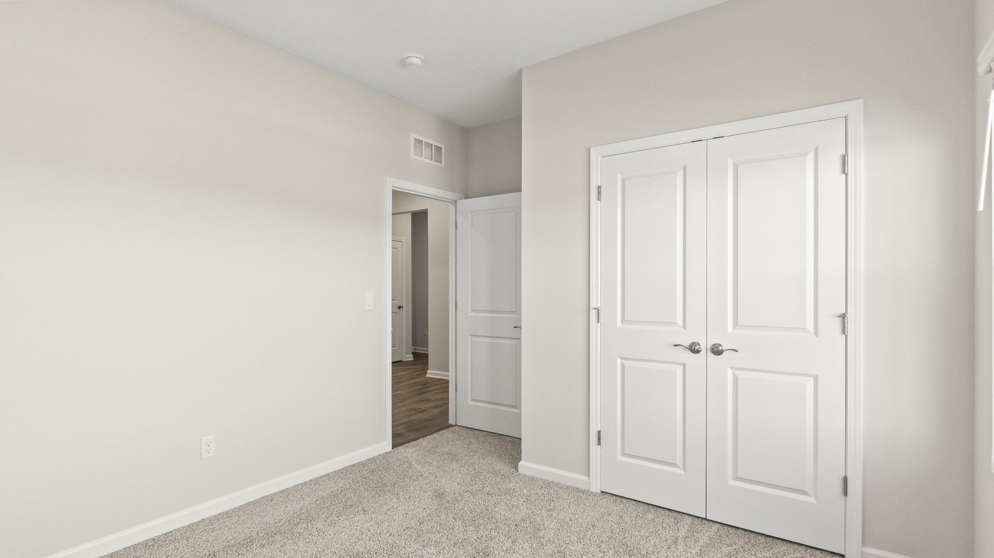 Carpeted bedroom looking into hallway with closet doors in frame.