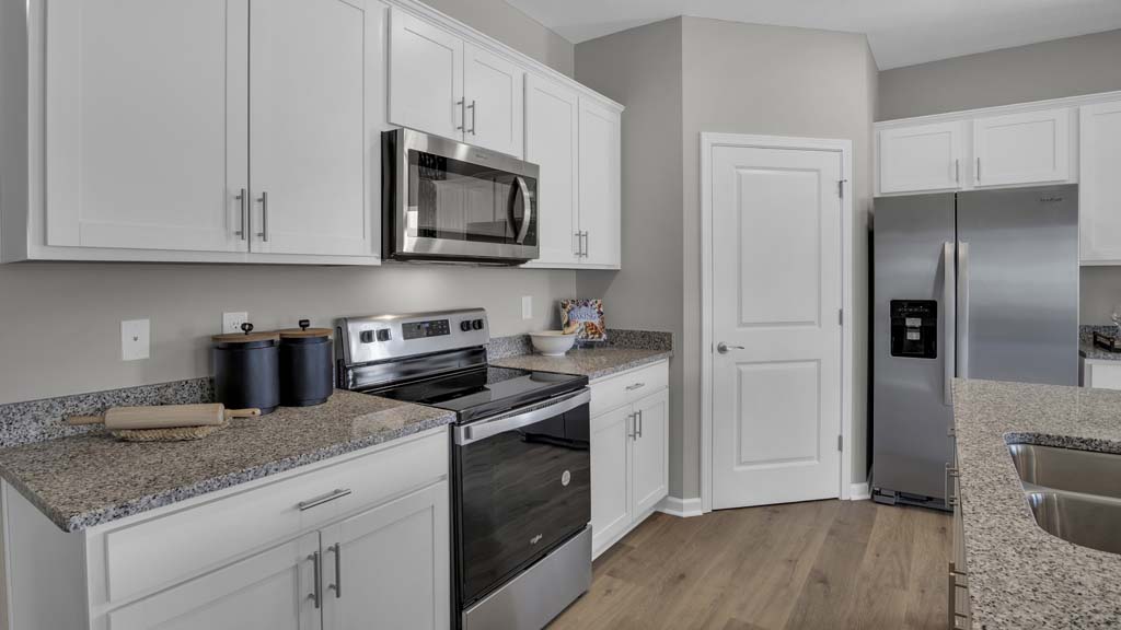 Kitchen with granite countertops and whirlpool stainless steel appliances with pantry door and white cabinets.