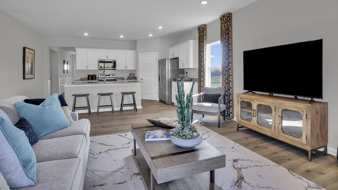 Living room with modern decorations, large flatscreen tv, and kitchen in background.