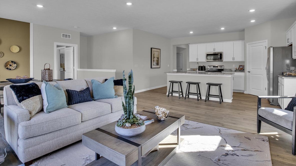 Living room with modern decorations, large flatscreen tv, and kitchen in background.
