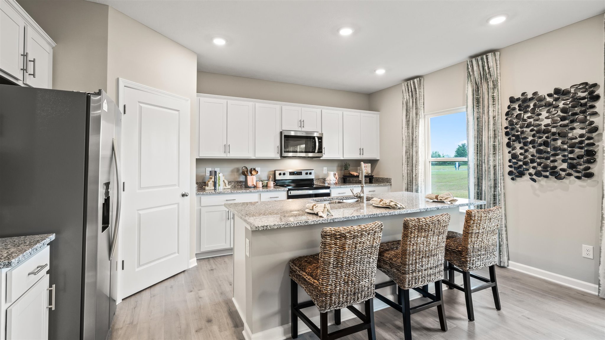 Full view of modern kitchen with granite countertops and white cabintrey with a large window.