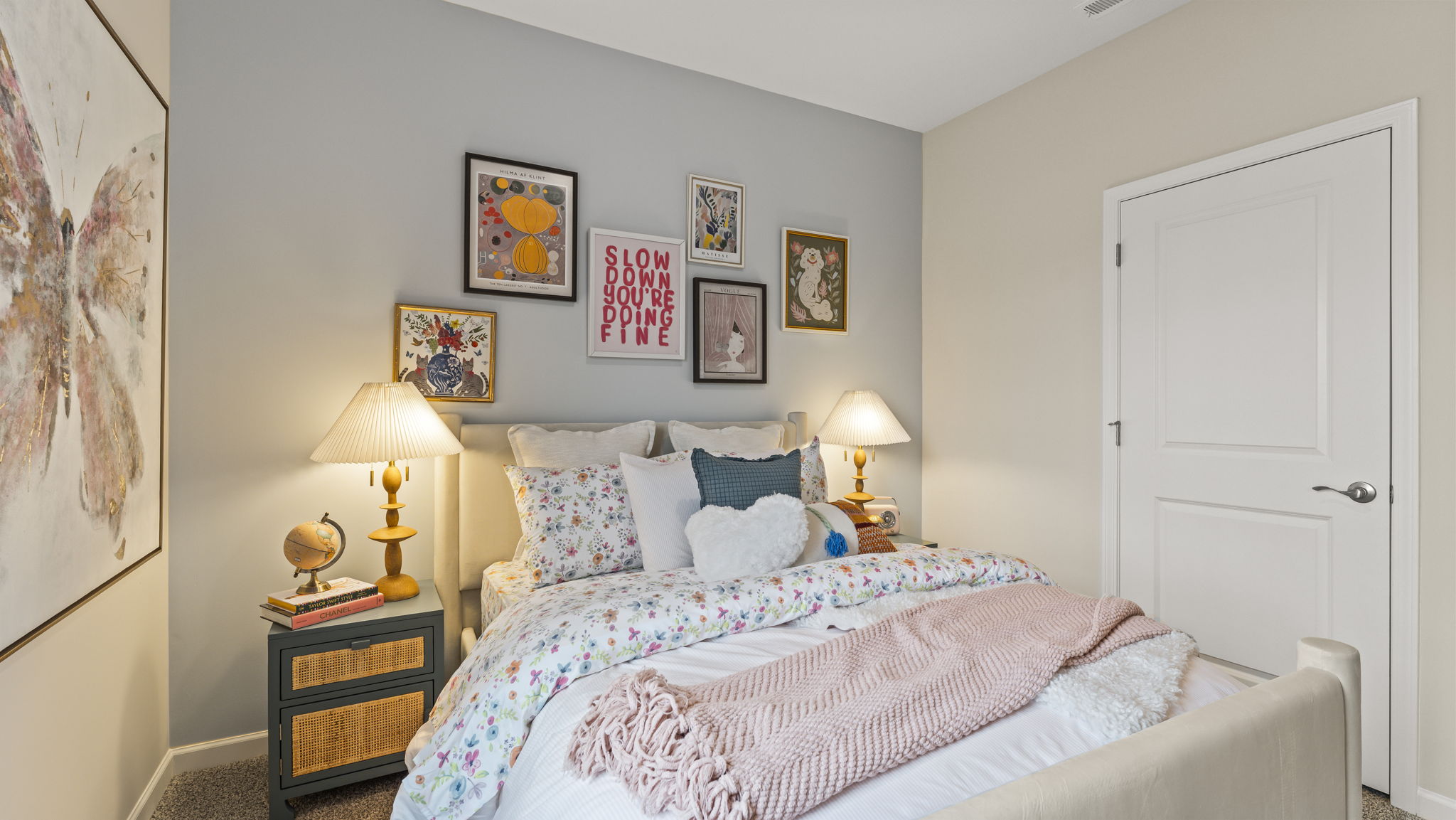 Three-quarter view of bed with floral bedding, warm art above the bed, and door to closet for storage space.