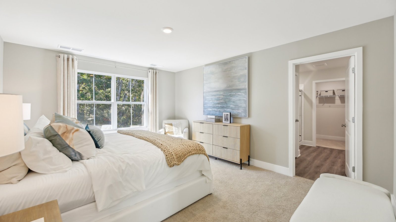 Primary bedroom with gorgeous white bed and modern decorations view into private bathroom.