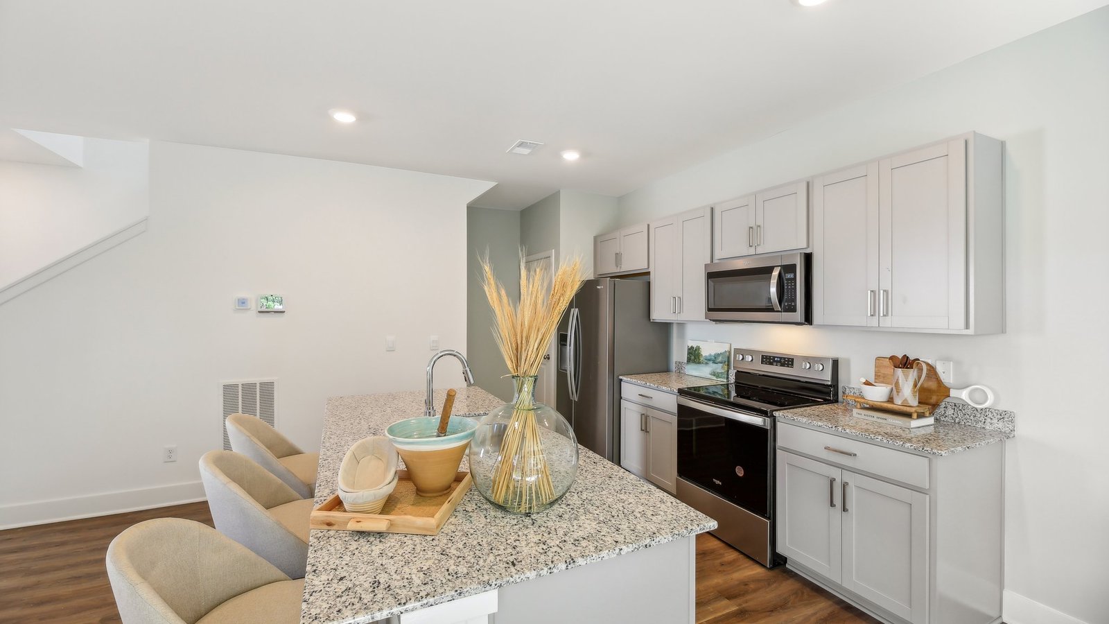 Kitchen with grey cabinets and stainless steel appliances and island with comfy chairs.
