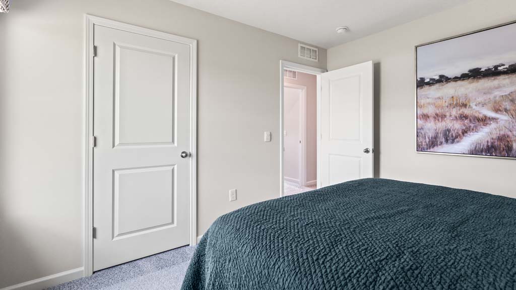 Corner view of bedroom with large dark green bed with view to hallway.
