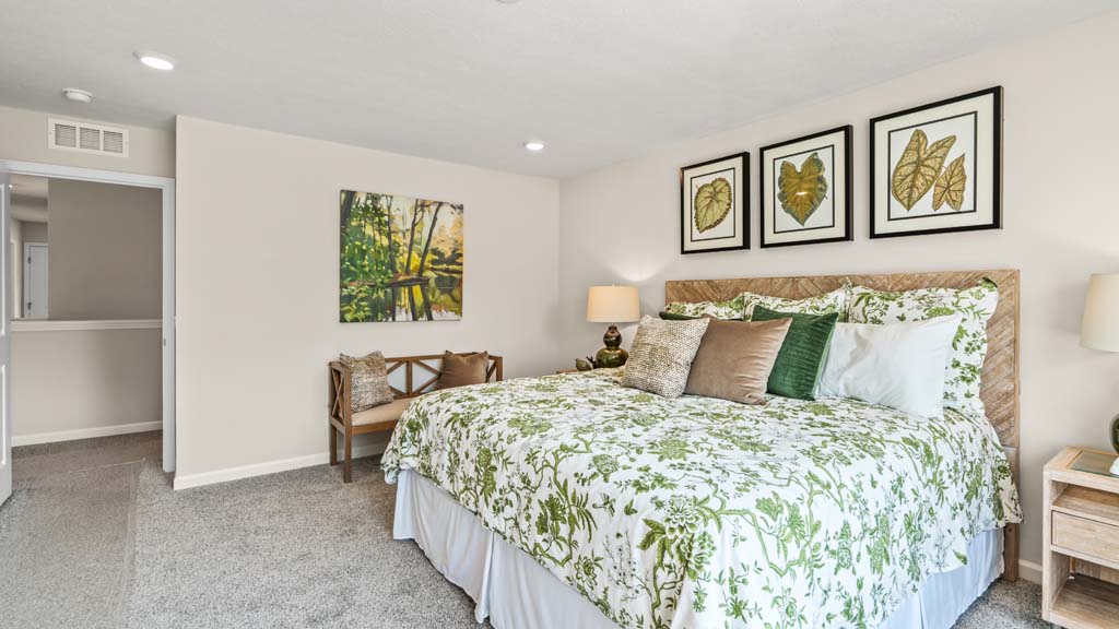 Primary bedroom with green décor and large bed with wooden accents and wooden bench.
