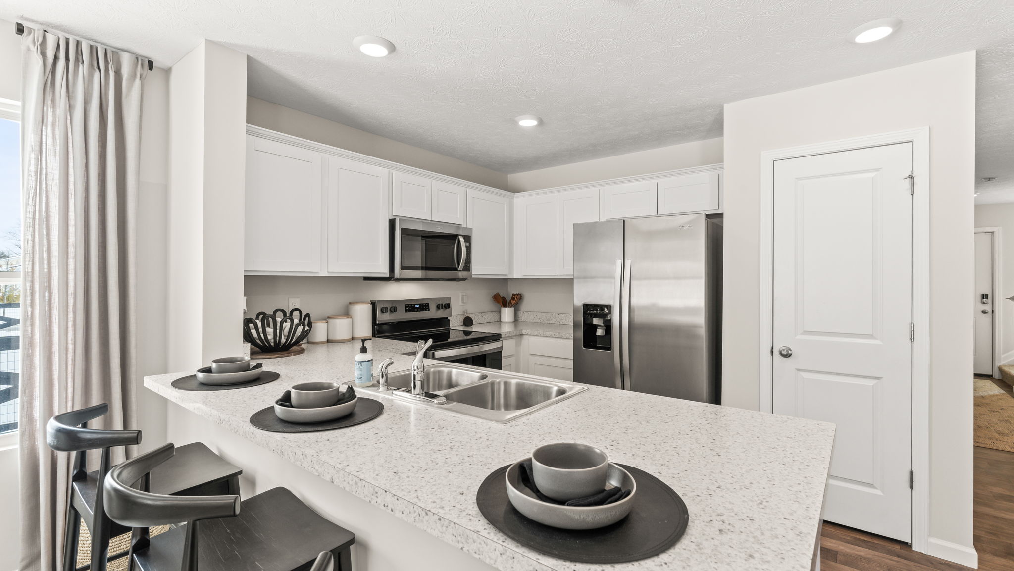 Townhome kitcen with bowls on the island, black wooden chairs, and stainless steel appliances