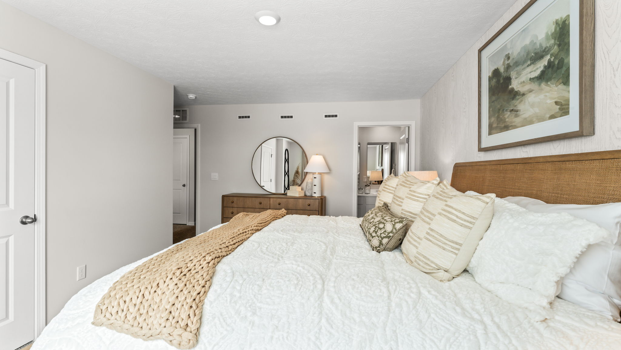 Closeup of the primary bed with light comforter and doorway to primary bathroom in the back