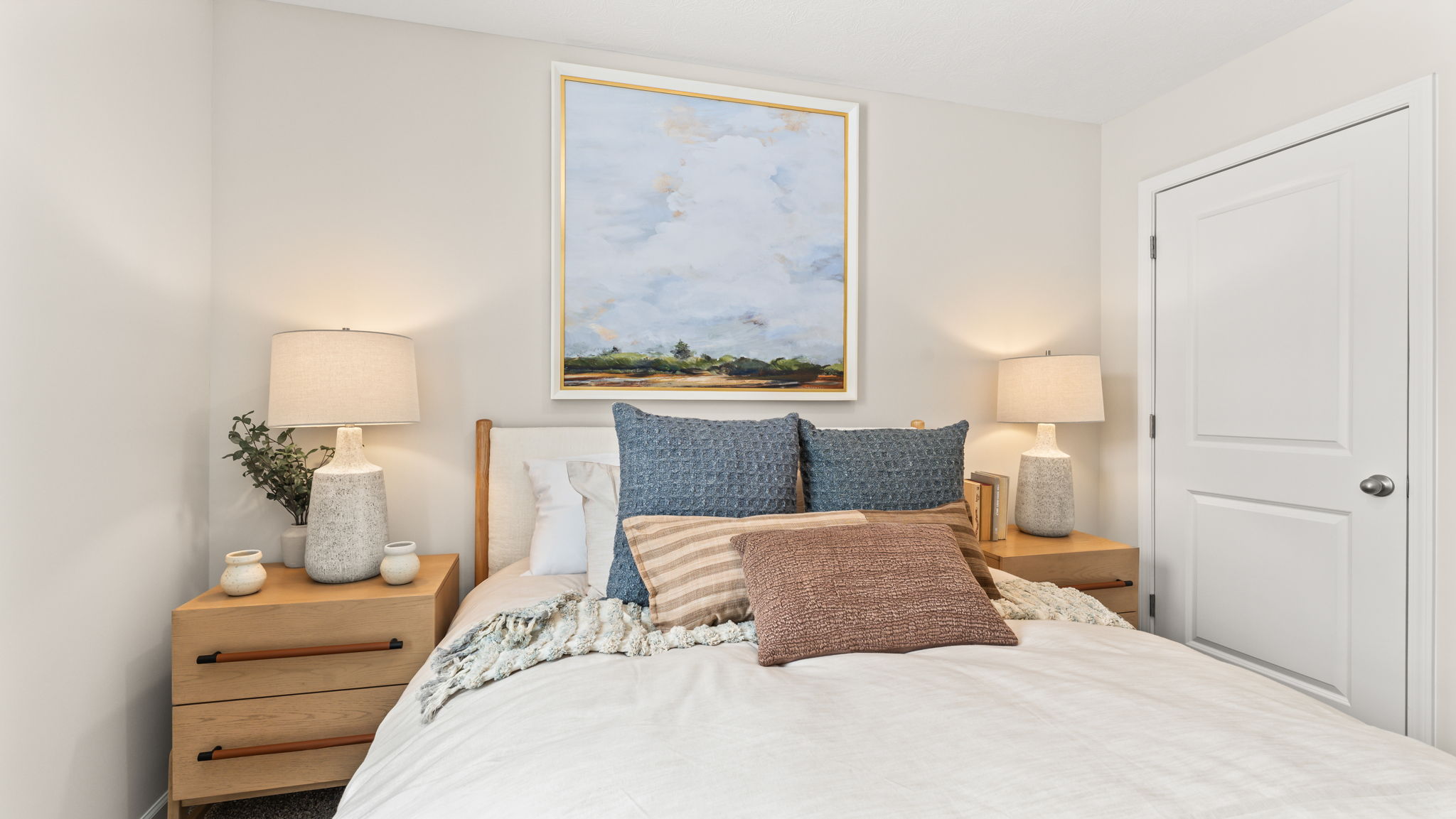 Closeup of bed with white comforter between two light wood nightstands
