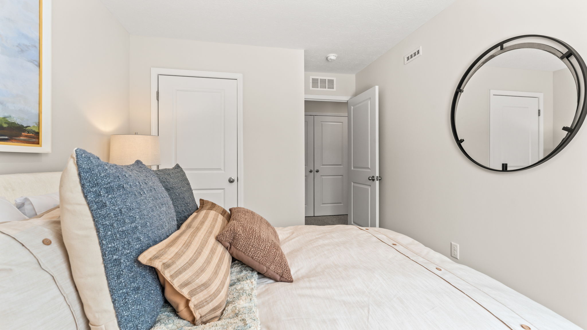 Side view of bed with door to closet, mirror on wall, and door to hallway in the back