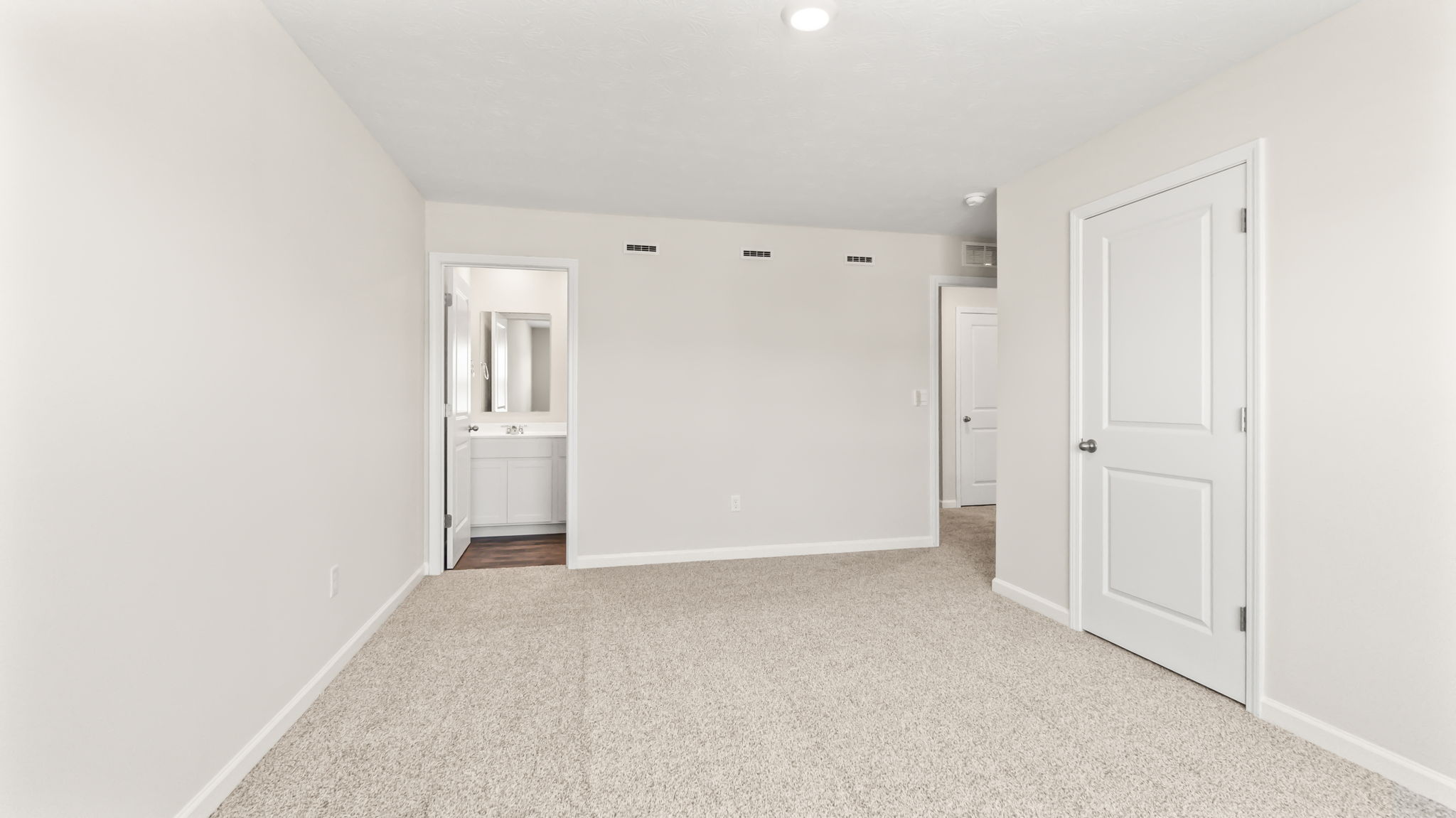Carpeted primary bedroom with door ot bathroom suite