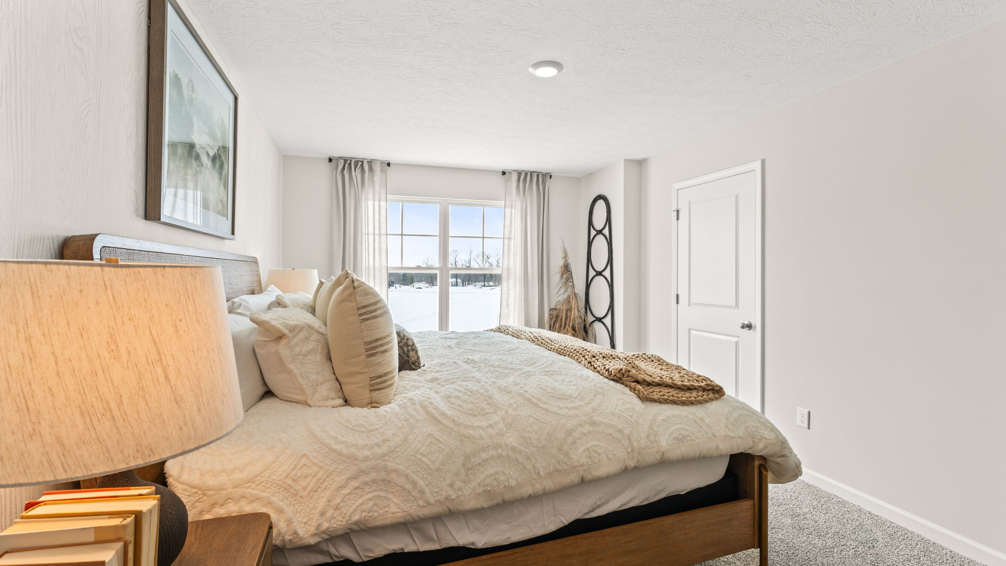Closeup of the primary bed with light comforter and door to walk-in closet in the back