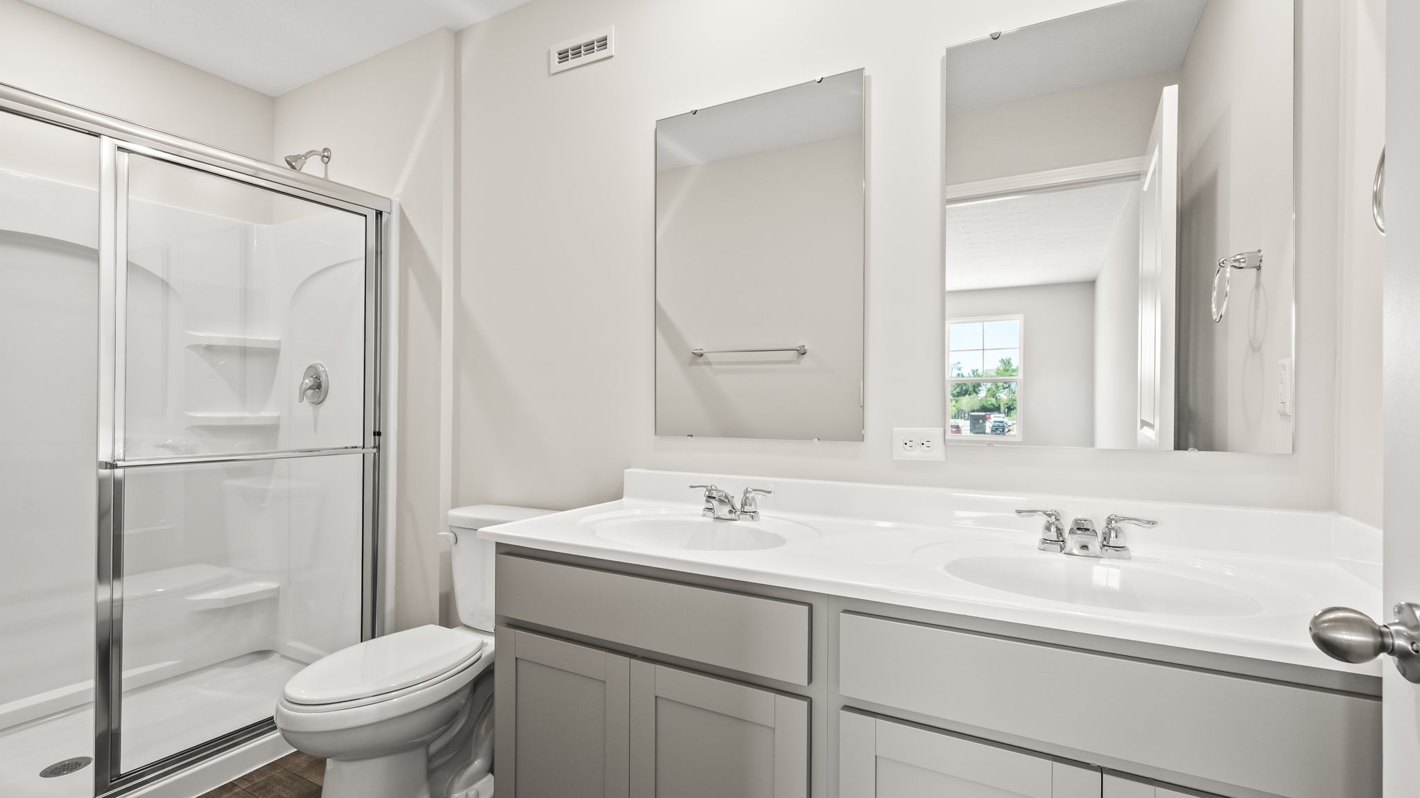 Primary bathroom suite with sliding glass door, toilet, and double sink vanity with mirrors