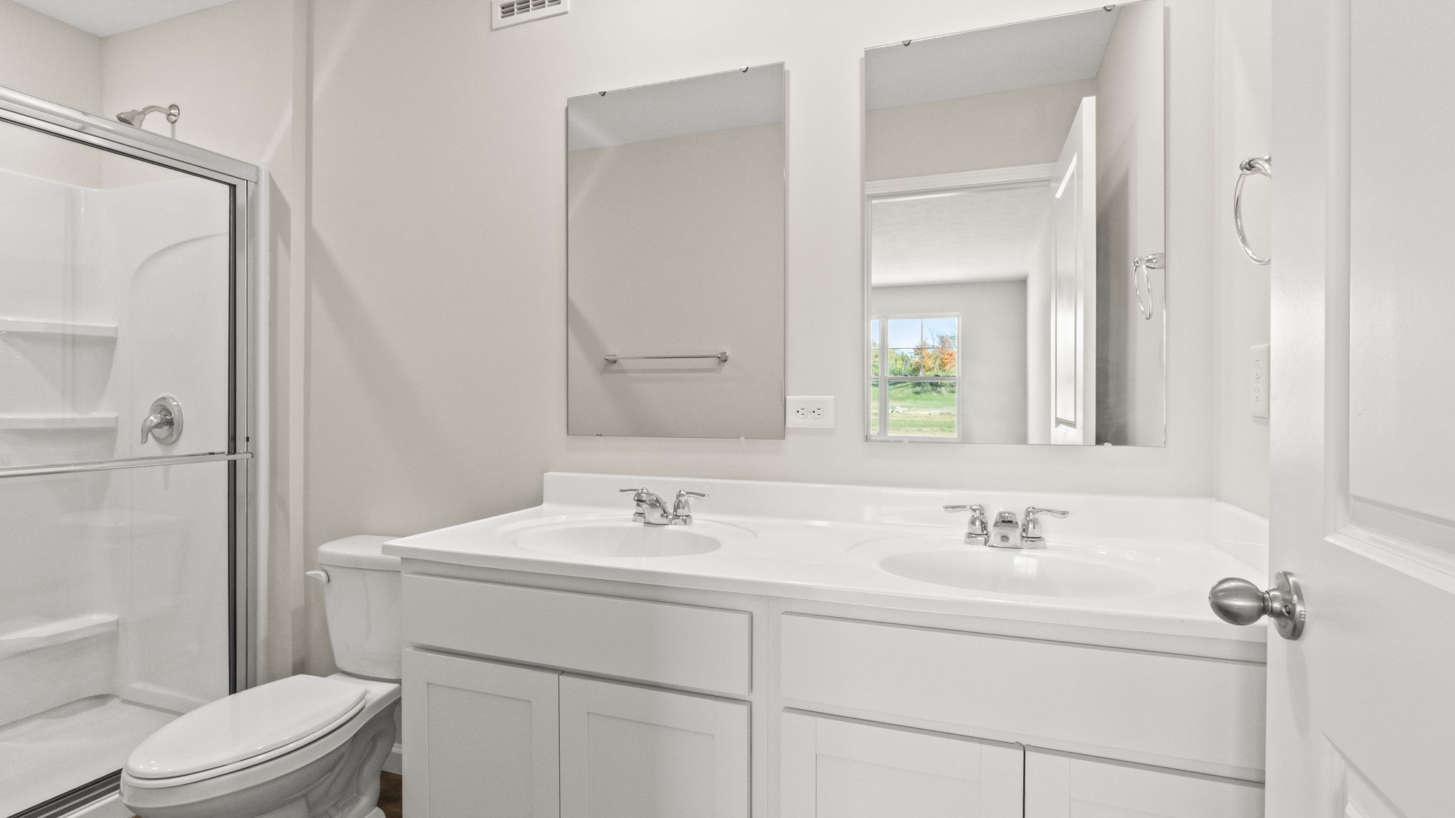 Dual-vanity sink and mirrors next to toilet and walk-in shower