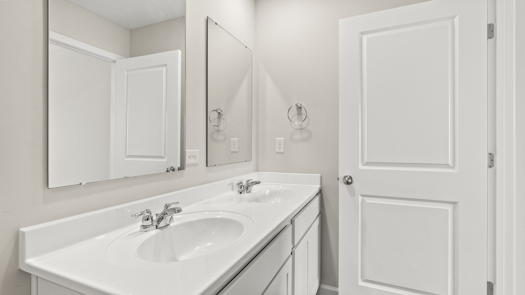 Closeup of dual-sink vanity with mirrors and door to primary bedroom