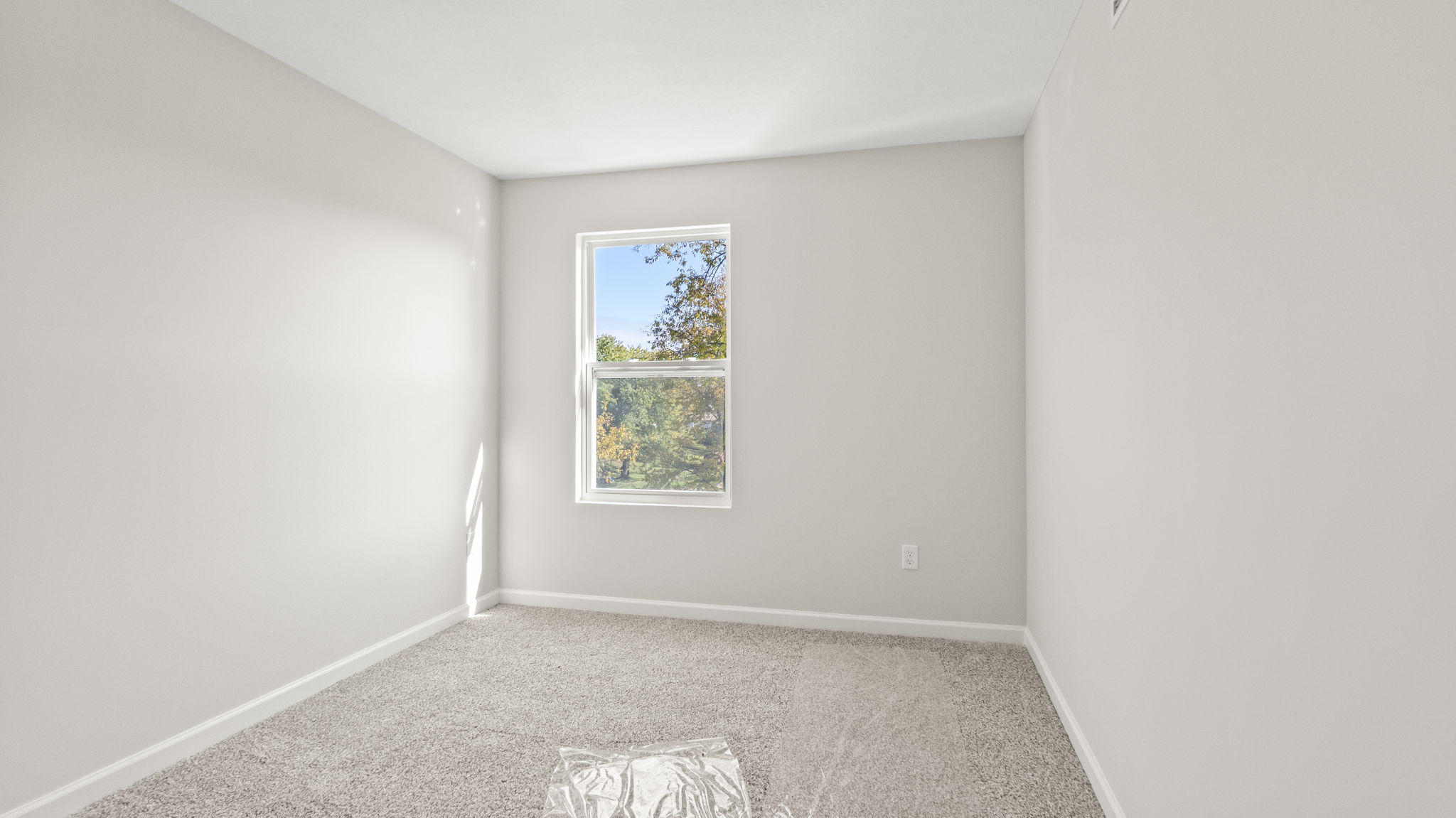 Carpeted bedroom with outlet and window.