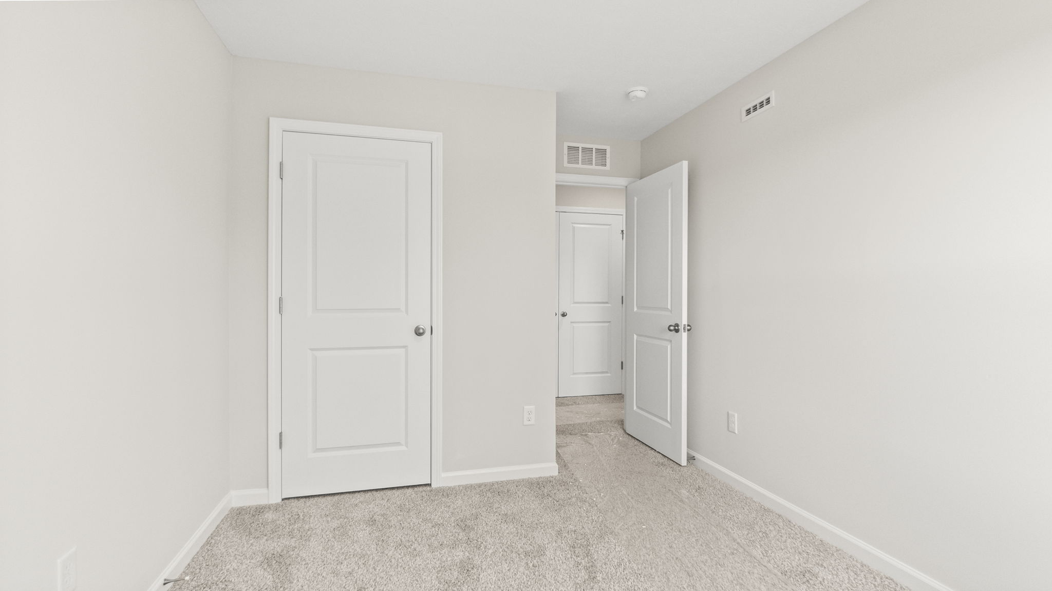 Carpeted bedroom with outlets, closet, and view of hallway.