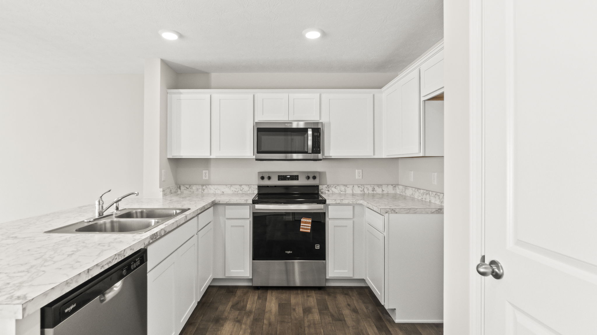 Side view of kitchen with laminate countertops, dishwasher, white cabinetry, sink, and stove.