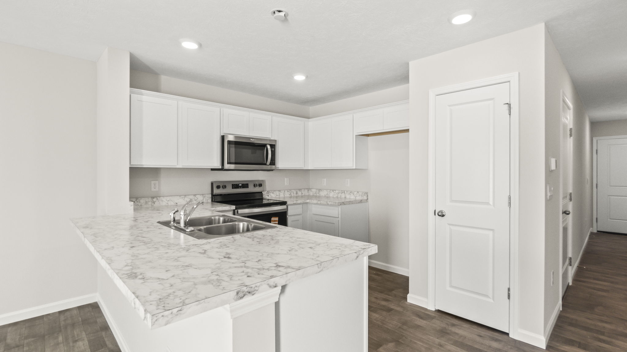 Three-quarter angle of kitchen with laminate countertops, appliances, white cabinetry, and door to pantry