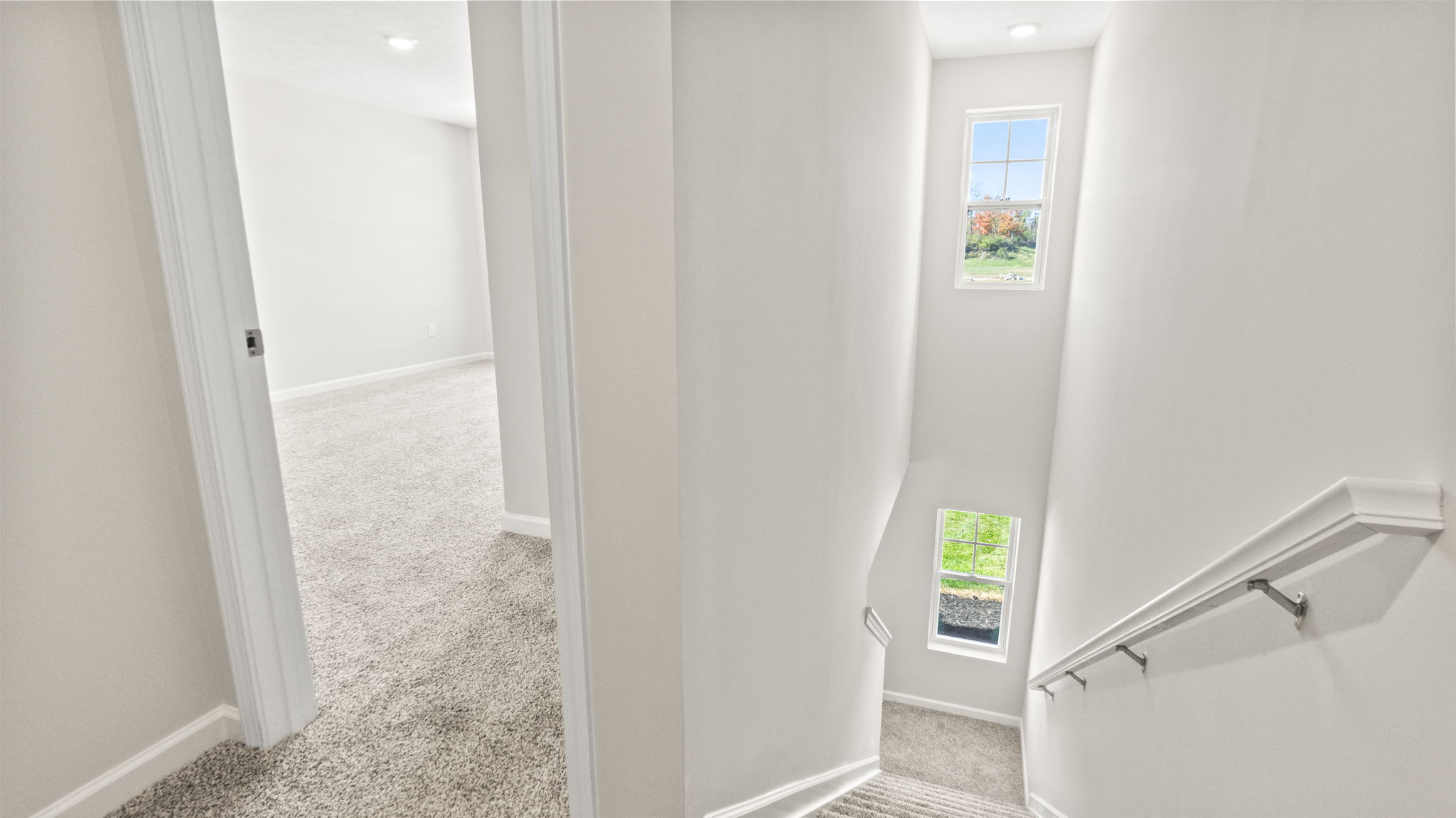 Upstairs looking down at carpeted stairs and into carpeted primary bedroom