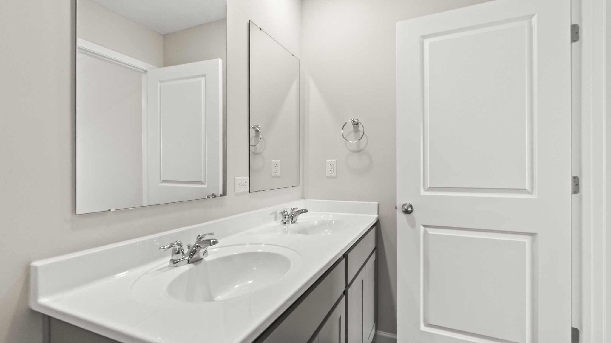 Closeup of dual-sink vanity with mirrors and door to primary bedroom