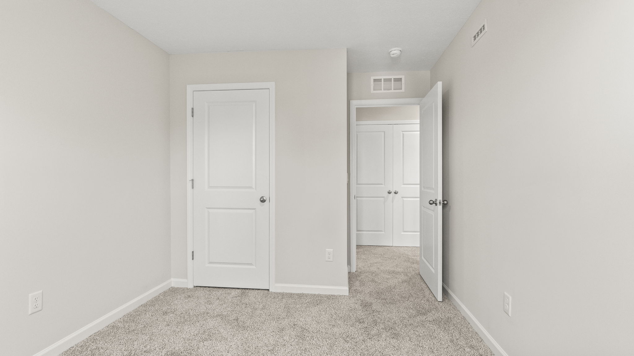 Carpeted bedroom with outlets, closet, and view of hallway.
