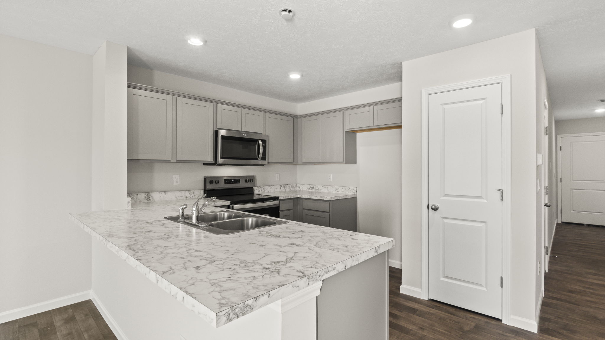 Three-quarter angle of kitchen with laminate countertops, appliances, white cabinetry, and door to pantry