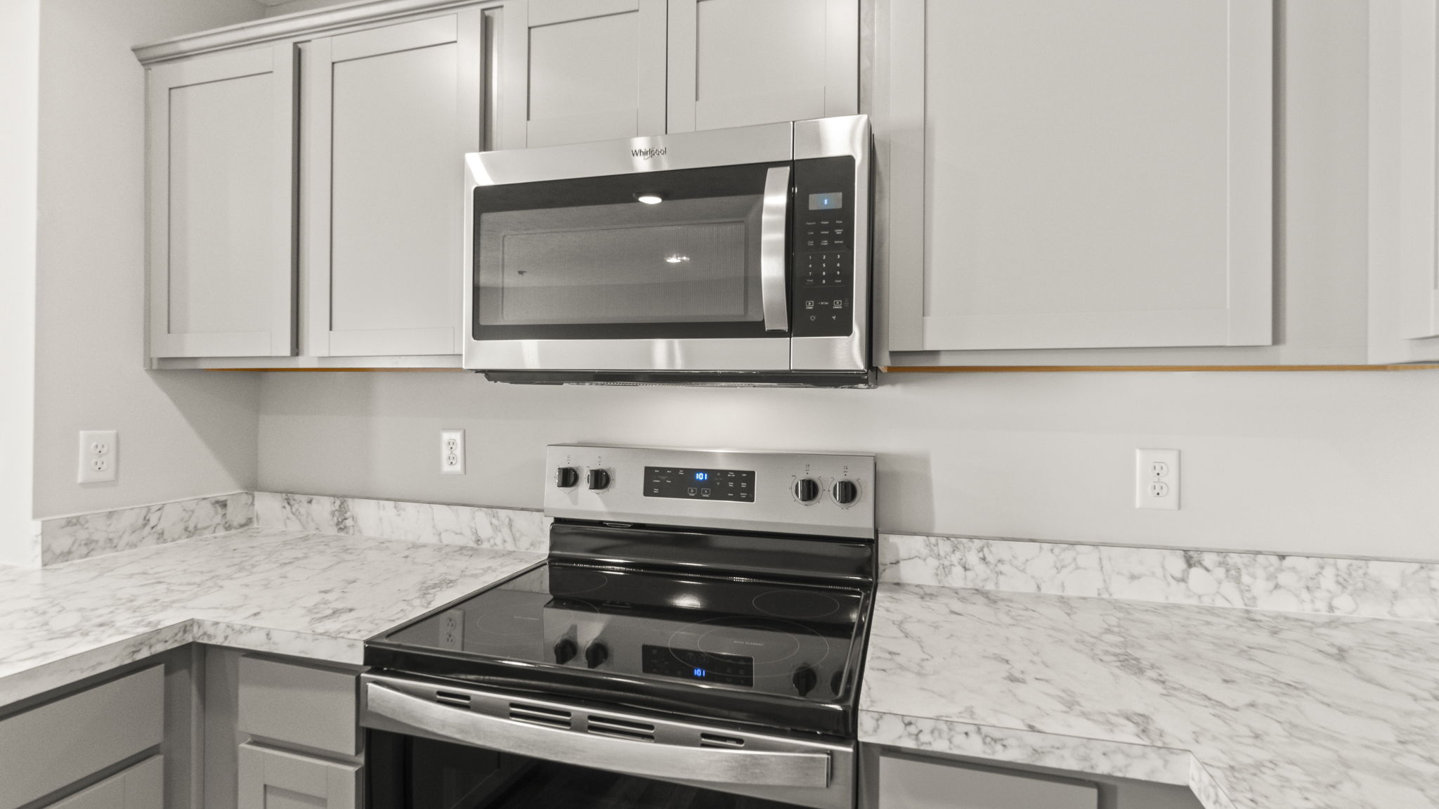 Closeup of stove and microwave between laminate countertops and white cabinets respectively.