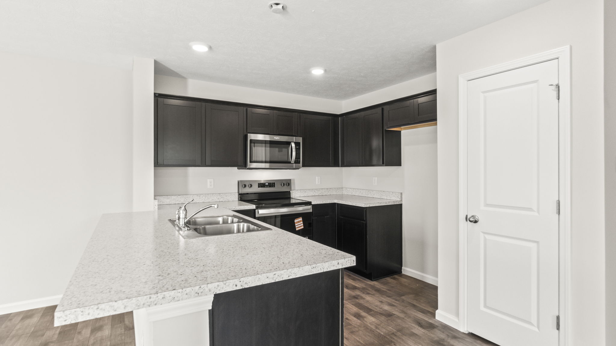 Three-quarter angle of kitchen with laminate countertops, appliances, woodgrain cabinetry, and door to pantry.
