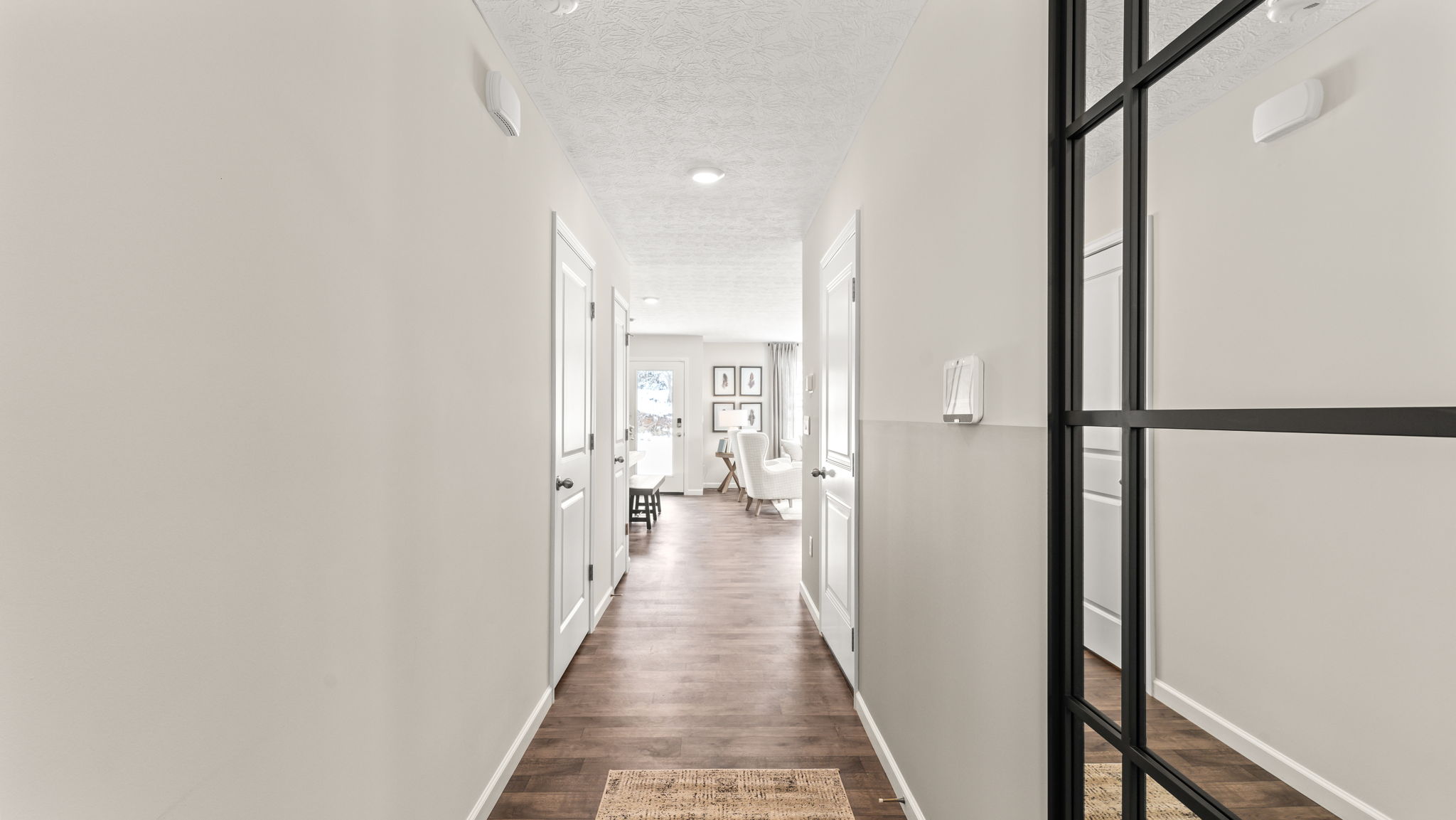 Hallway coming from the kitchen with doors to the bathroom and storage. A Large mirror with black framing is positioned on the right of the wall